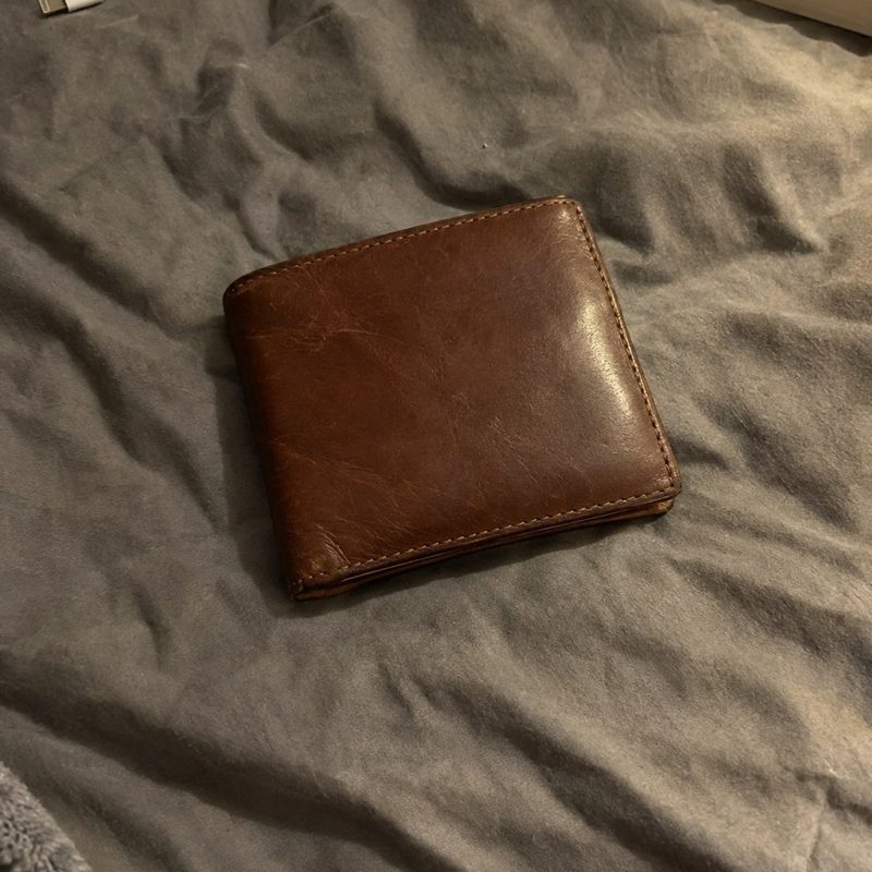 A brown leather wallet on a rumpled bed sheet